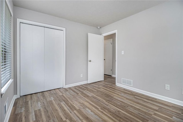 unfurnished bedroom featuring baseboards, visible vents, wood finished floors, and a closet
