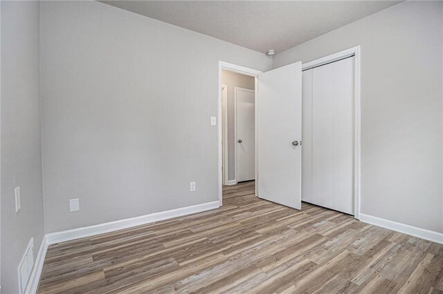unfurnished bedroom with baseboards, visible vents, light wood finished floors, and a closet