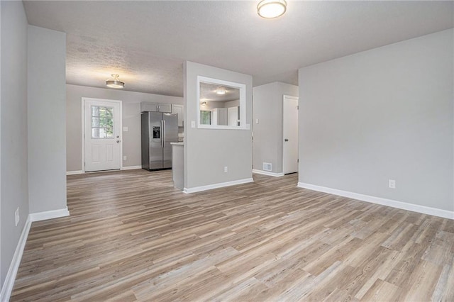 unfurnished living room featuring baseboards, a textured ceiling, light wood finished floors, and visible vents