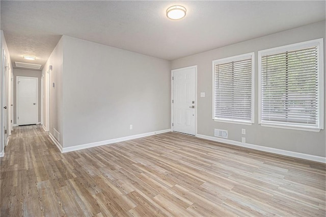 empty room with baseboards, attic access, light wood-type flooring, and visible vents