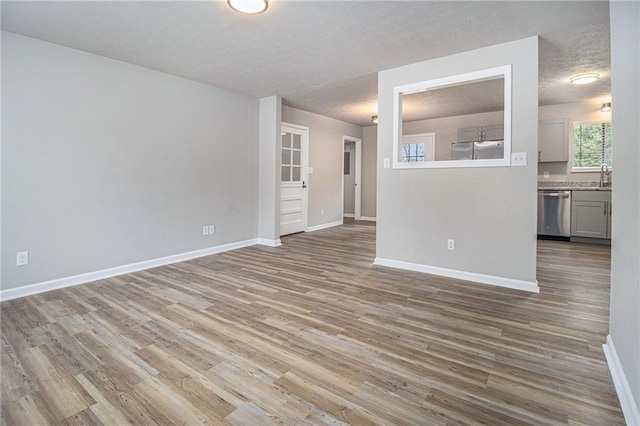 unfurnished living room featuring baseboards, a sink, a textured ceiling, and wood finished floors