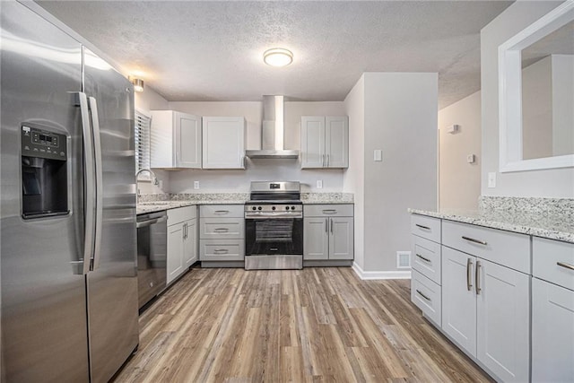kitchen featuring light stone countertops, wall chimney exhaust hood, a sink, light wood-style flooring, and stainless steel appliances