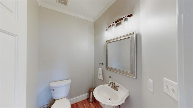 half bath with a sink, crown molding, toilet, wood finished floors, and baseboards