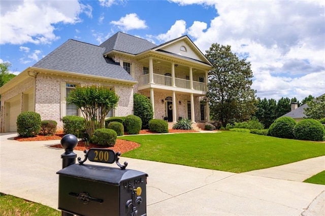 greek revival house featuring a balcony, brick siding, a front yard, roof with shingles, and an attached garage