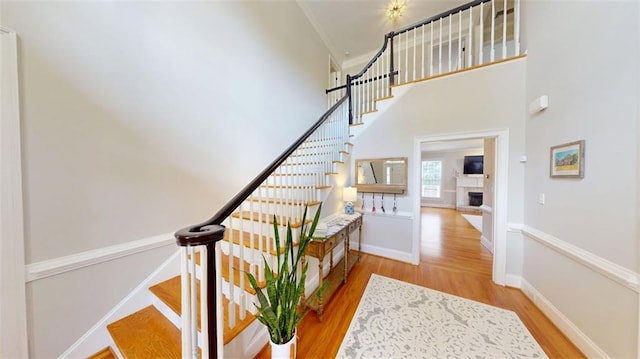 staircase featuring wood finished floors, a towering ceiling, baseboards, and a fireplace with raised hearth