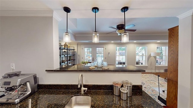 kitchen featuring a ceiling fan, crown molding, dark stone countertops, a sink, and a peninsula