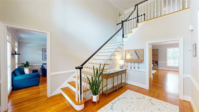 stairway with wood finished floors, ornamental molding, a high ceiling, and baseboards