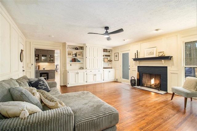 living room with built in shelves, ceiling fan, a textured ceiling, and light wood-type flooring