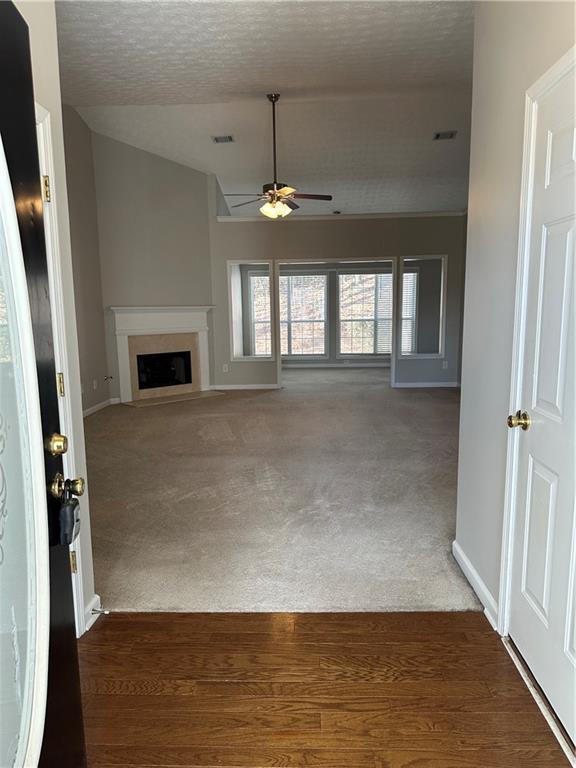 unfurnished living room featuring lofted ceiling, dark carpet, a textured ceiling, and ceiling fan