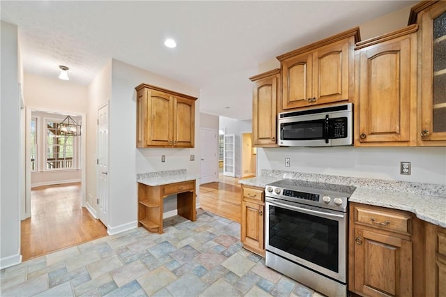 kitchen featuring stone finish floor, light stone counters, stainless steel appliances, glass insert cabinets, and baseboards