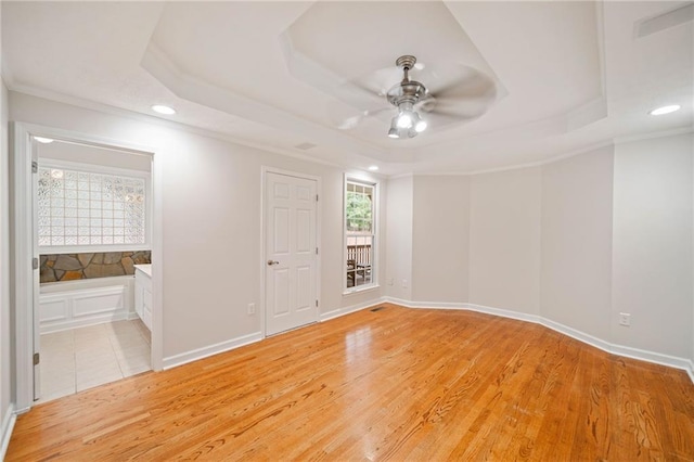 unfurnished room with crown molding, a raised ceiling, and light wood-style floors