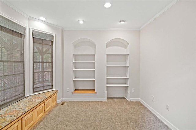 interior space featuring built in shelves, crown molding, baseboards, and carpet floors