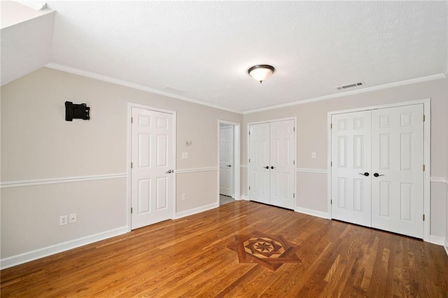 unfurnished bedroom featuring visible vents, crown molding, baseboards, multiple closets, and wood finished floors