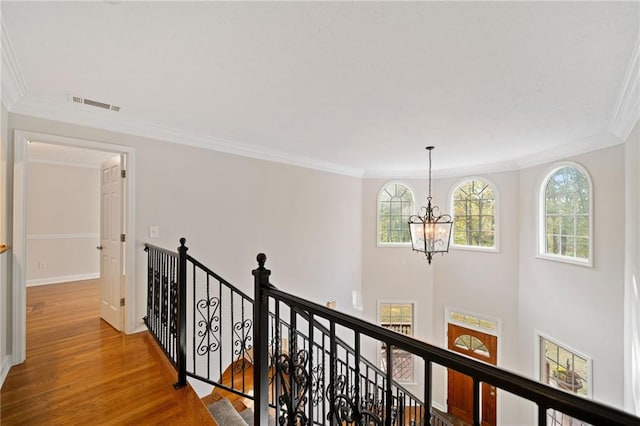 hall featuring an upstairs landing, visible vents, a healthy amount of sunlight, and wood finished floors