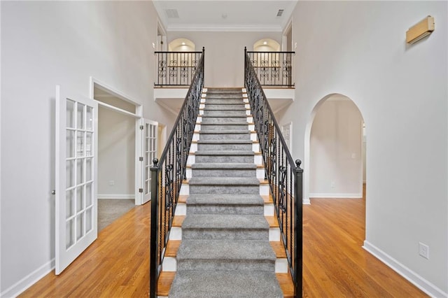 stairway with crown molding, wood finished floors, arched walkways, and a towering ceiling