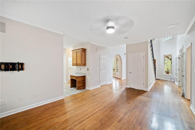 unfurnished living room with light wood-style flooring, arched walkways, crown molding, baseboards, and ceiling fan