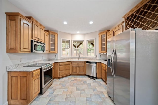 kitchen featuring light stone countertops, recessed lighting, a sink, stainless steel appliances, and glass insert cabinets