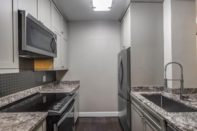 kitchen featuring tasteful backsplash, a sink, appliances with stainless steel finishes, dark wood finished floors, and light stone countertops