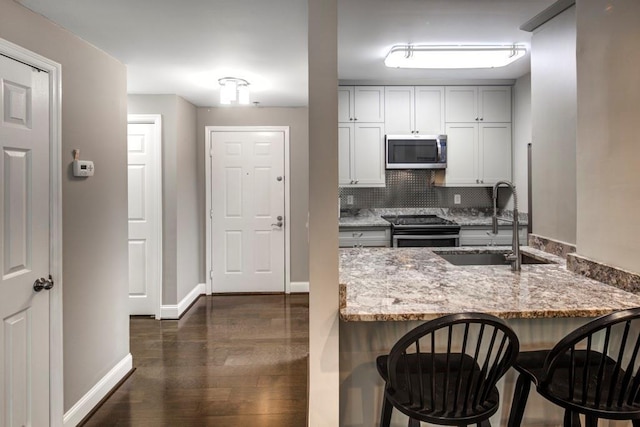 kitchen with a breakfast bar area, a sink, light stone countertops, and stainless steel appliances