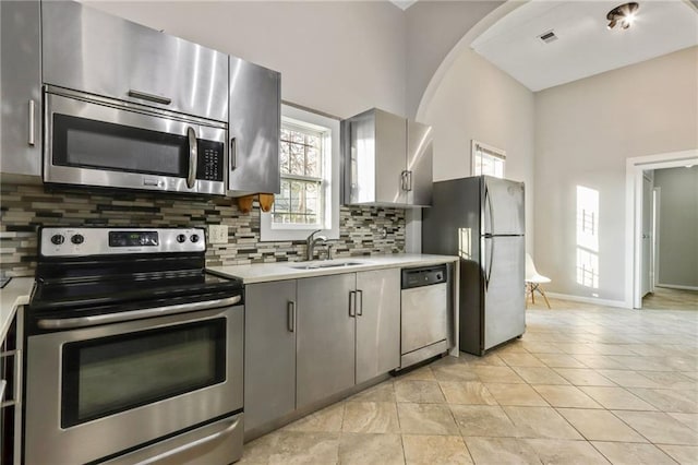 kitchen featuring gray cabinets, appliances with stainless steel finishes, sink, decorative backsplash, and light tile patterned floors