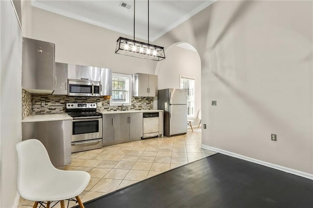 kitchen featuring pendant lighting, crown molding, gray cabinets, stainless steel appliances, and decorative backsplash