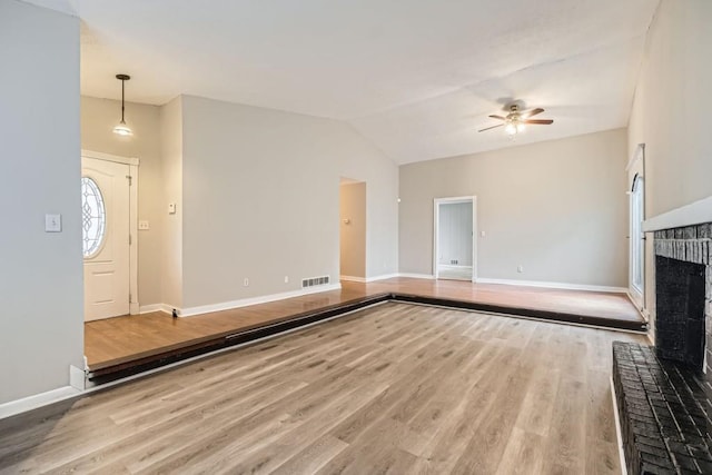 unfurnished living room with lofted ceiling, a brick fireplace, ceiling fan, and light wood-type flooring