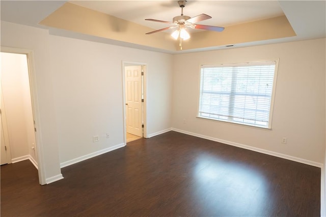 unfurnished room with a raised ceiling, dark hardwood / wood-style floors, and ceiling fan