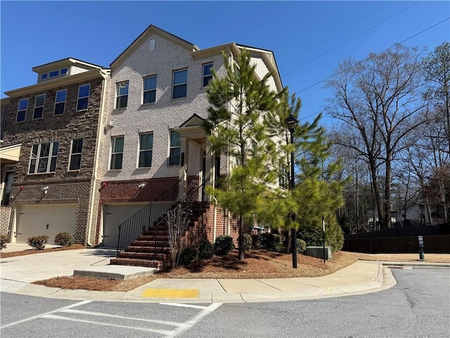 townhome / multi-family property with a garage, concrete driveway, brick siding, and stairs