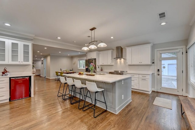 kitchen with dishwashing machine, visible vents, a kitchen breakfast bar, stainless steel refrigerator with ice dispenser, and wall chimney range hood