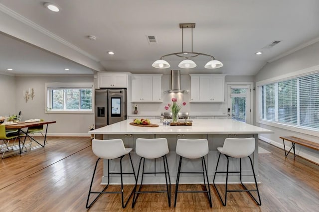 kitchen with stainless steel fridge, a large island with sink, wall chimney exhaust hood, and white cabinetry