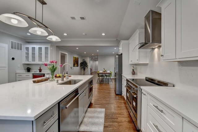 kitchen with a sink, stainless steel appliances, white cabinets, and wall chimney range hood