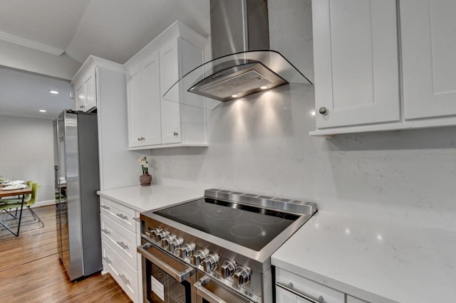 kitchen with light wood-style flooring, ornamental molding, white cabinetry, stainless steel appliances, and wall chimney range hood