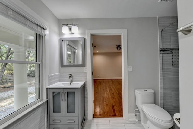 bathroom with visible vents, toilet, vanity, and a tile shower