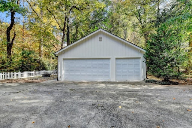 detached garage with fence and a view of trees