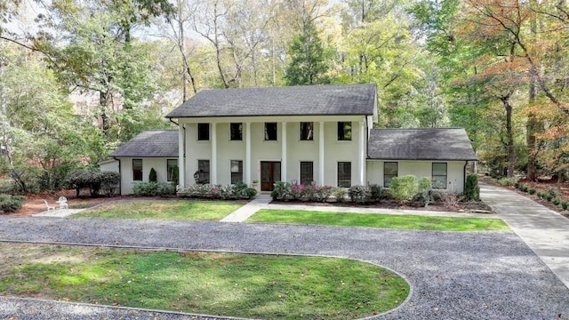 neoclassical / greek revival house with a front yard, a wooded view, driveway, and roof with shingles