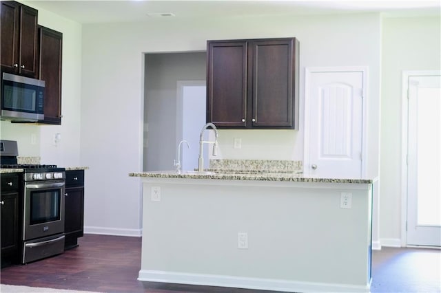 4417 Belcamp Rd, Fairburn, GA 30213 - kitchen featuring appliances with stainless steel finishes, dark brown cabinets, light stone counters, dark wood-type flooring, and a center island with sink