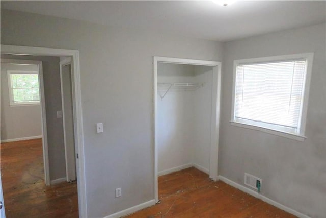 unfurnished bedroom featuring multiple windows, dark wood-type flooring, and a closet