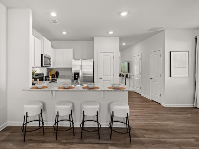 kitchen with dark wood-type flooring, kitchen peninsula, stainless steel appliances, a breakfast bar, and white cabinetry