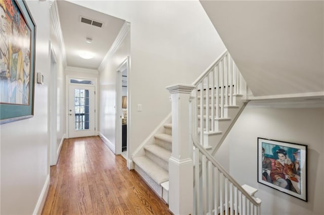 hall featuring visible vents, crown molding, baseboards, stairs, and wood finished floors