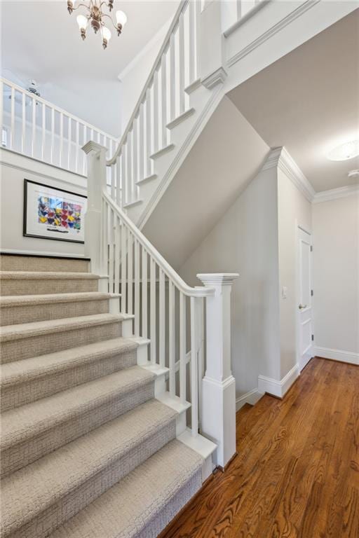 stairway with wood finished floors, baseboards, an inviting chandelier, ornamental molding, and a towering ceiling