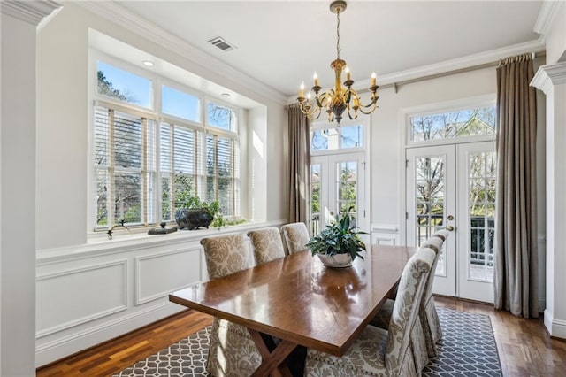 dining space with a chandelier, visible vents, a decorative wall, and ornamental molding