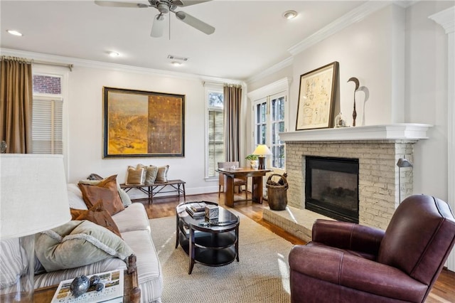 living room with visible vents, a ceiling fan, wood finished floors, a fireplace, and crown molding