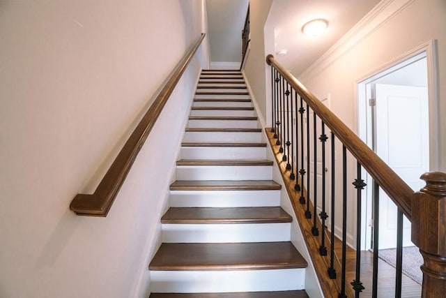 staircase with wood finished floors and ornamental molding