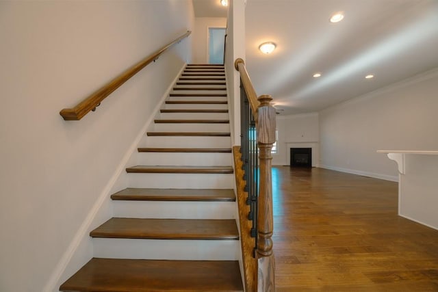 stairway featuring baseboards, ornamental molding, recessed lighting, a fireplace, and wood finished floors