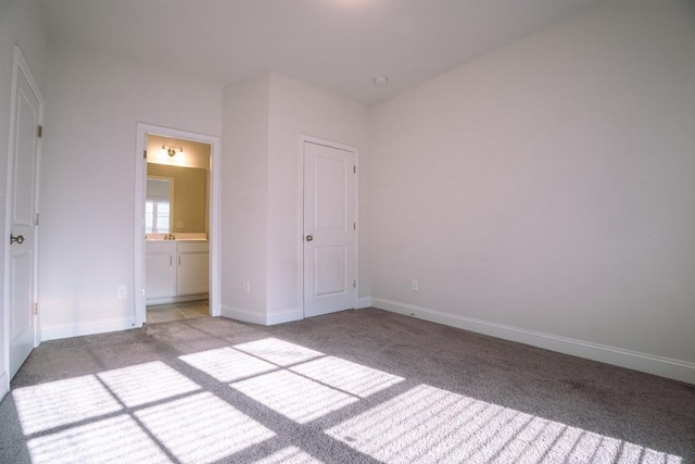 unfurnished bedroom with light colored carpet, ensuite bath, baseboards, and a sink