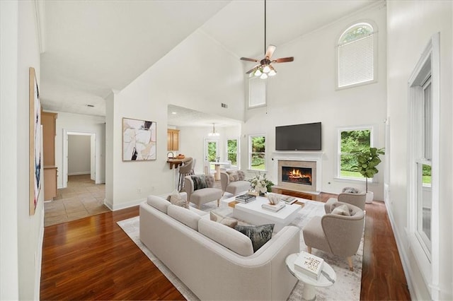 living area featuring a healthy amount of sunlight, a warm lit fireplace, a towering ceiling, and dark wood-style flooring