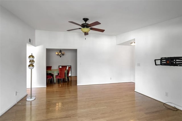 empty room featuring ceiling fan with notable chandelier and wood-type flooring