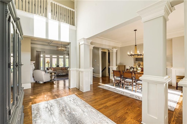 foyer with a chandelier, ornate columns, dark wood-type flooring, and crown molding