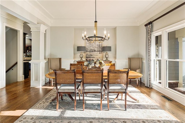 dining room featuring ornate columns, crown molding, wood-type flooring, and an inviting chandelier