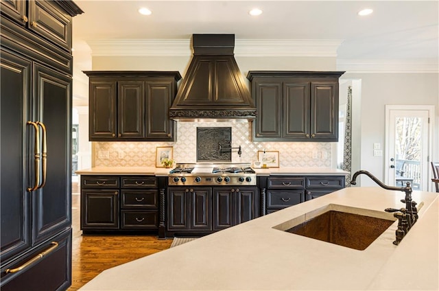 kitchen with custom exhaust hood, paneled built in fridge, sink, decorative backsplash, and stainless steel gas cooktop